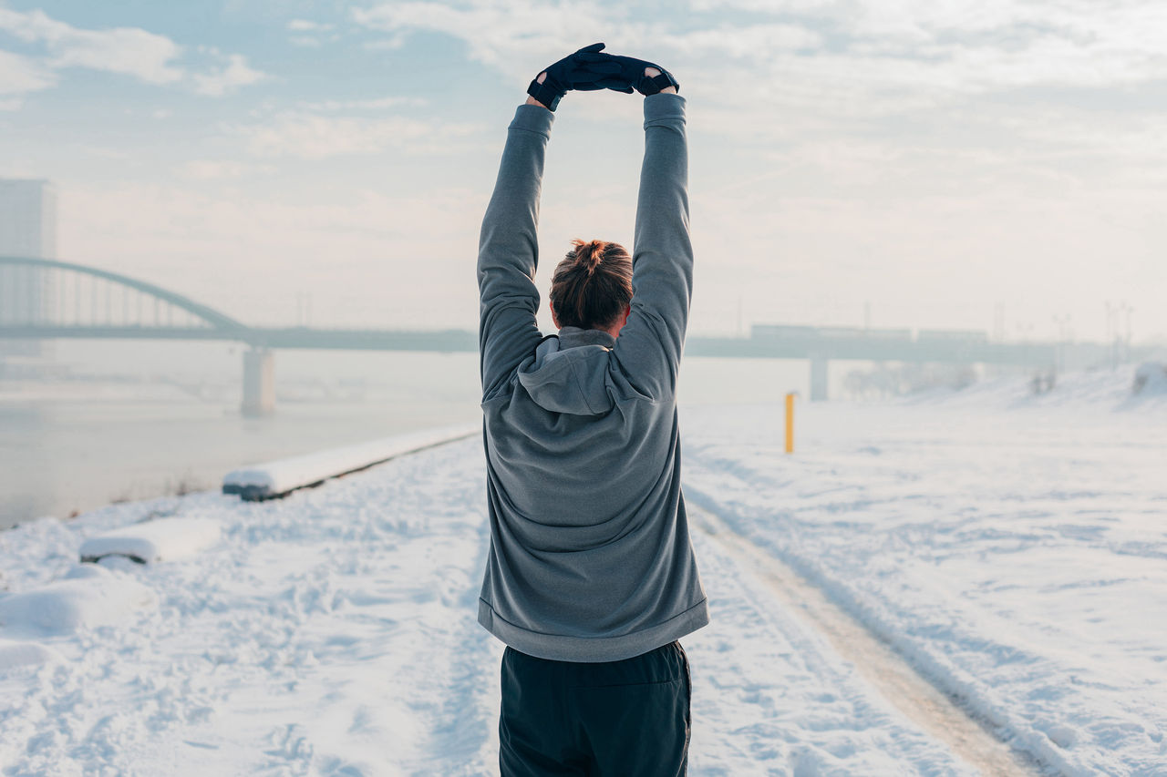 Back view of an attractive man standing outdoors, stretching, preparing for running on a sunny winter day